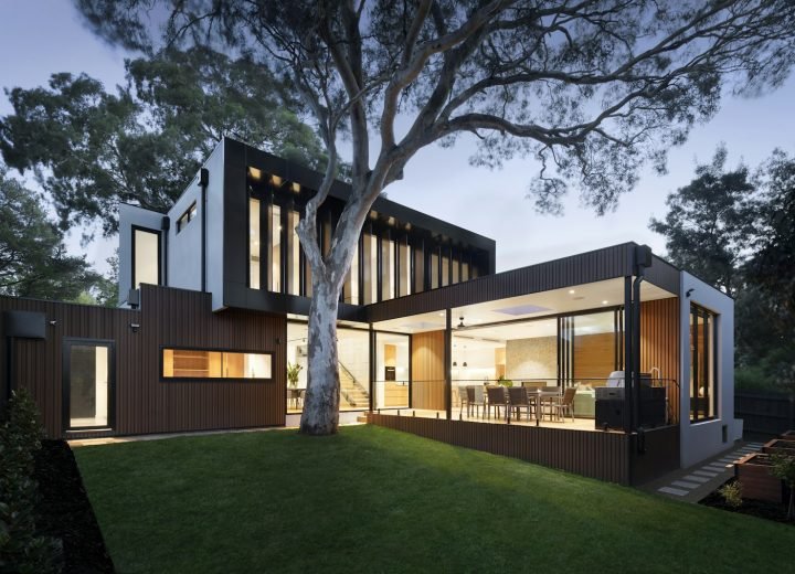 Modern house with lit windows and a lawn at dusk